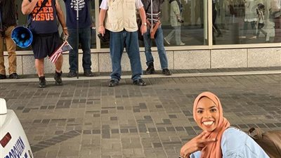 “بعلامة النصر وابتسامة”.. صورة لفتاة مسلمة أمام مظاهرة للعنصرية في الخارج تحولها لبطلة (صور)