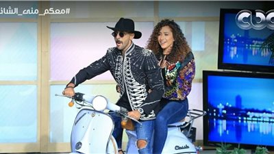 كعادته الغريبة.. حسن أبو الروس وزوجته يدخلان ستوديو برنامج منى الشاذلي بـ «موتوسيكل»